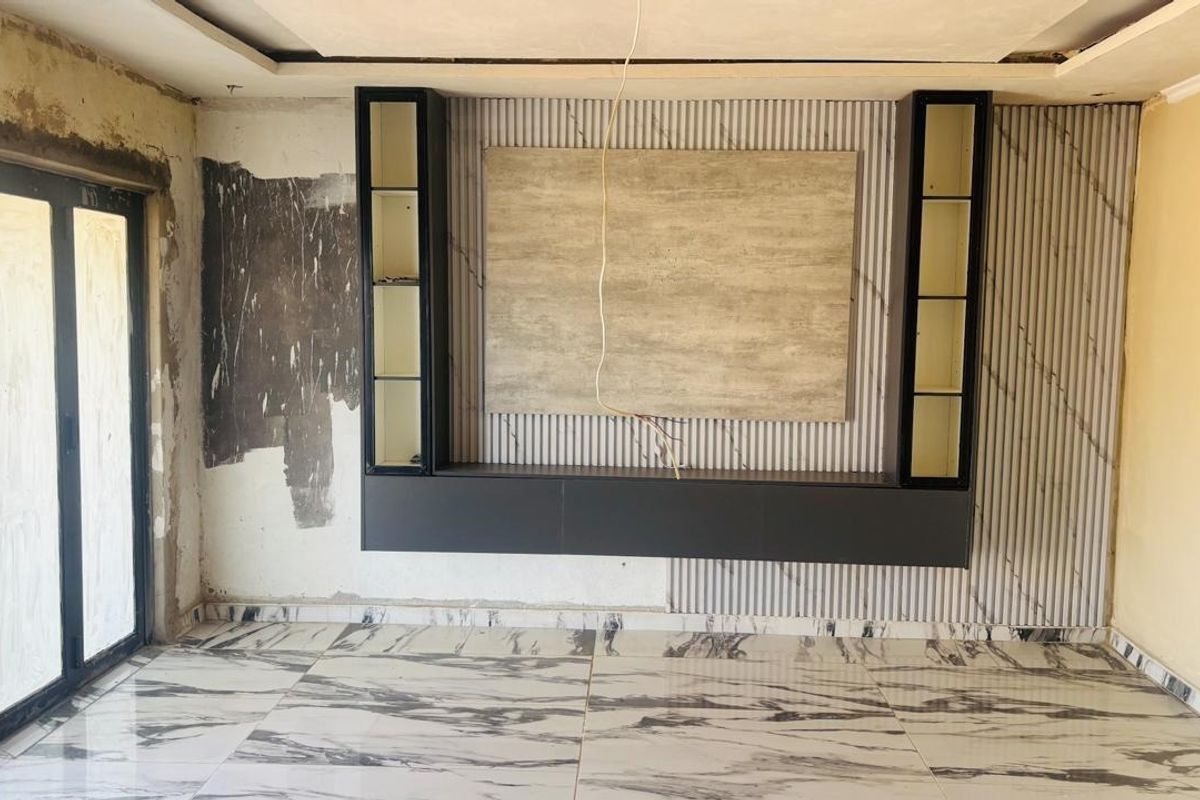 Living room featuring a modern built-in media unit, marble-look floor tiles, and bi-fold doors, currently undergoing renovation with unfinished wall surfaces.