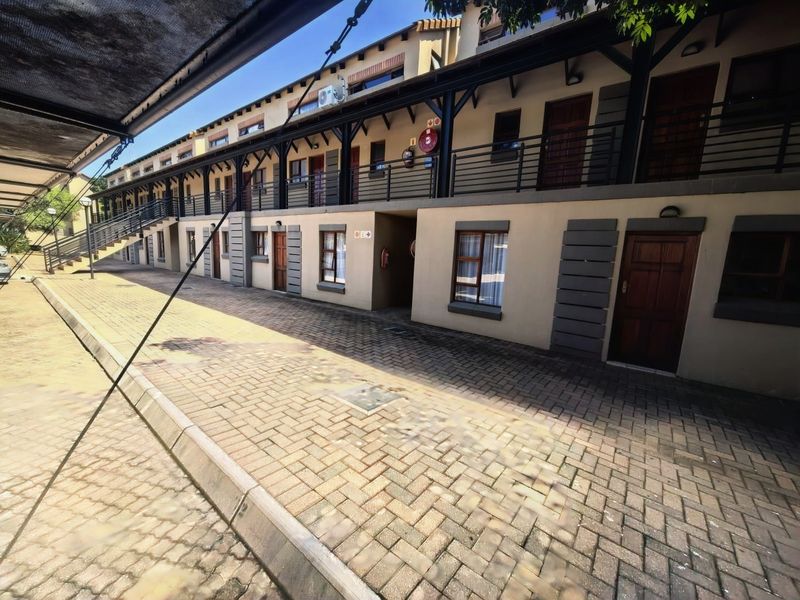 Exterior view of an apartment complex featuring a paved driveway, covered walkways, and multiple unit entrances with timber doors and metal balcony railings.