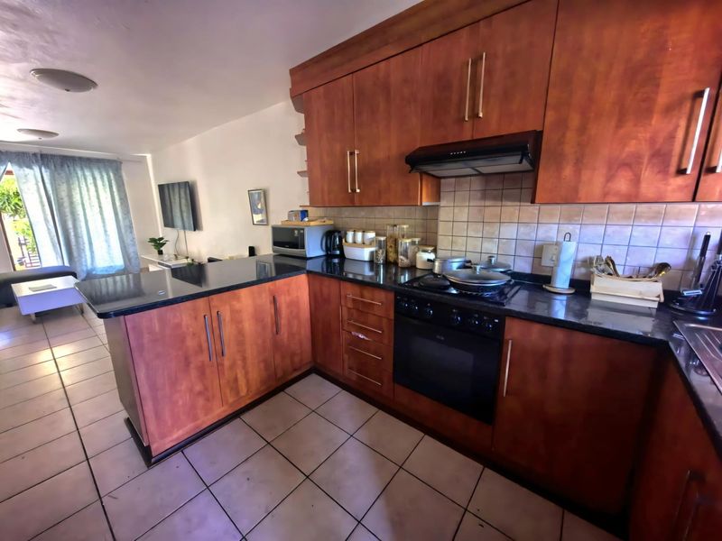 Open-plan kitchen featuring wooden cabinetry, granite countertops, and built-in appliances, seamlessly flowing into the adjacent living area with tiled flooring throughout.