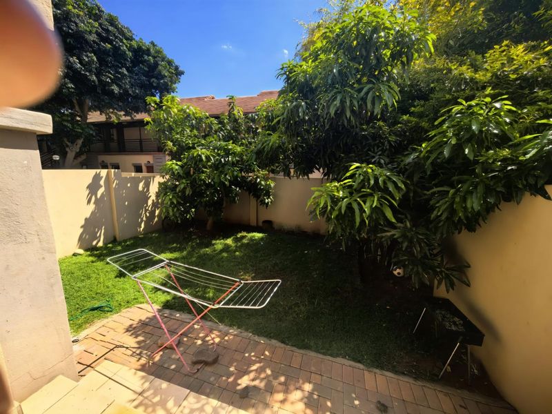 A private rear garden area featuring a paved patio section, established trees, and a boundary wall.