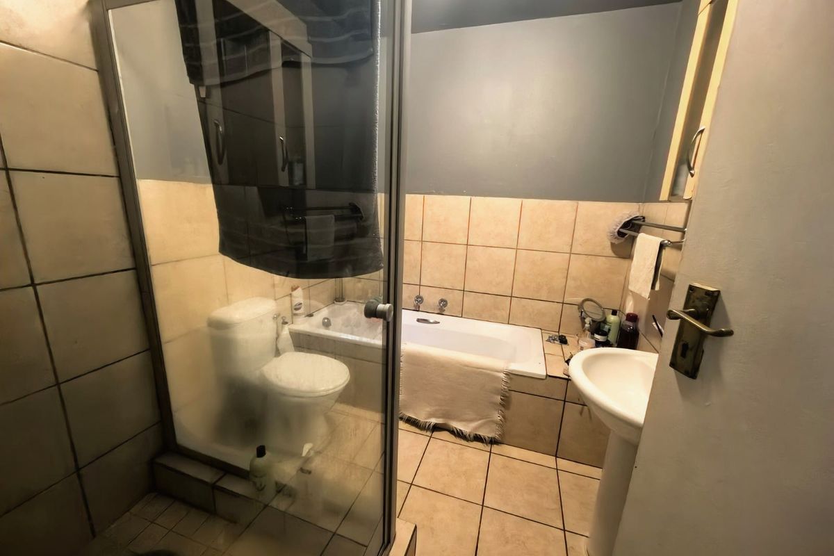 A functional bathroom featuring a shower enclosure, bathtub, pedestal sink, and toilet with neutral tiled finishes.
