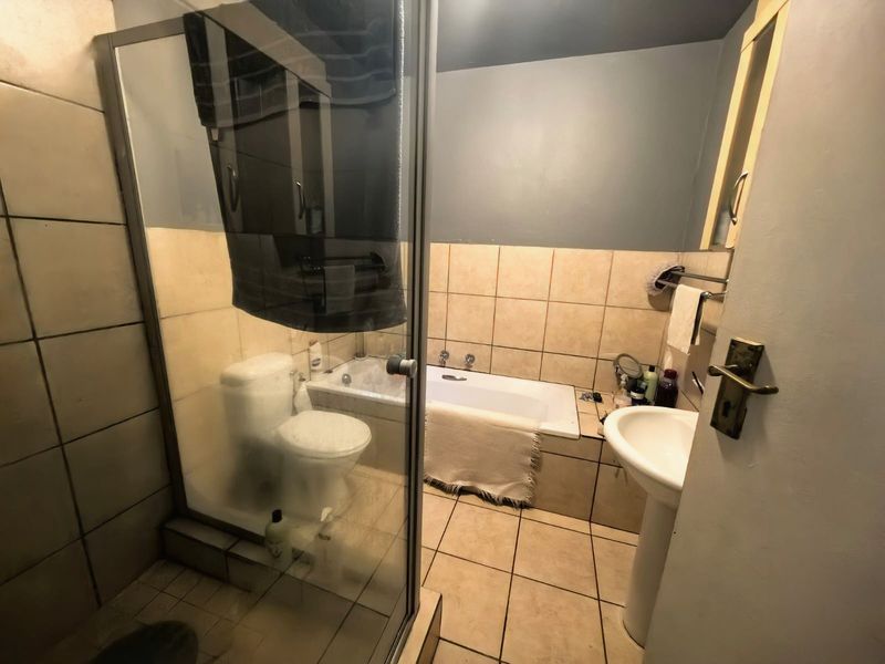 A functional bathroom featuring a shower enclosure, bathtub, pedestal sink, and toilet with neutral tiled finishes.