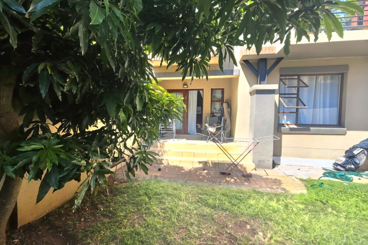Rear exterior view of the apartment featuring a paved patio area, sliding glass doors, and access to a small garden space.