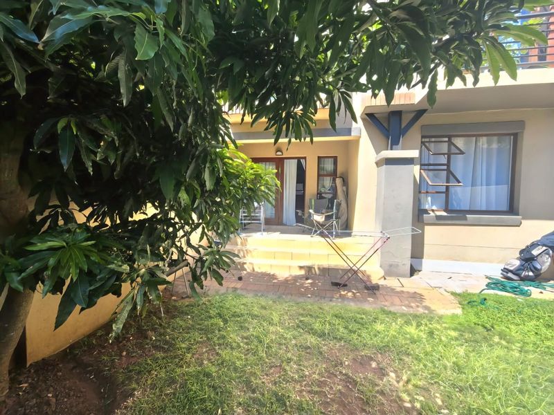 Rear exterior view of the apartment featuring a paved patio area, sliding glass doors, and access to a small garden space.