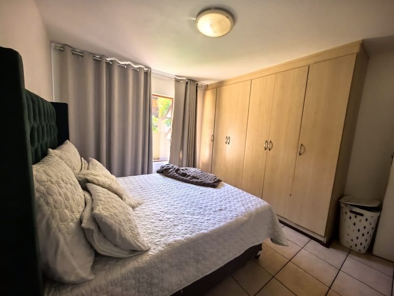 A functional bedroom featuring built-in wooden cupboards, tiled flooring, and a window with curtains, providing ample storage and natural light.