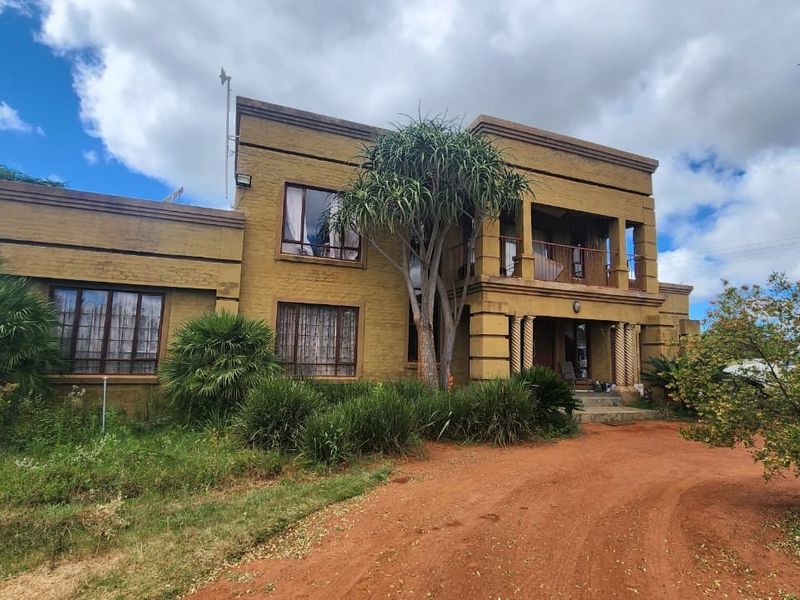 Front elevation of a double-storey brick residence featuring a balcony, columns, and a large driveway on a small holding property.