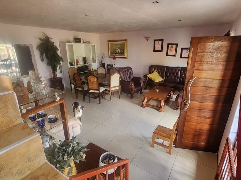 Spacious open-plan living and dining area featuring tiled flooring, recessed lighting, and a prominent stone-clad staircase leading to the upper level.