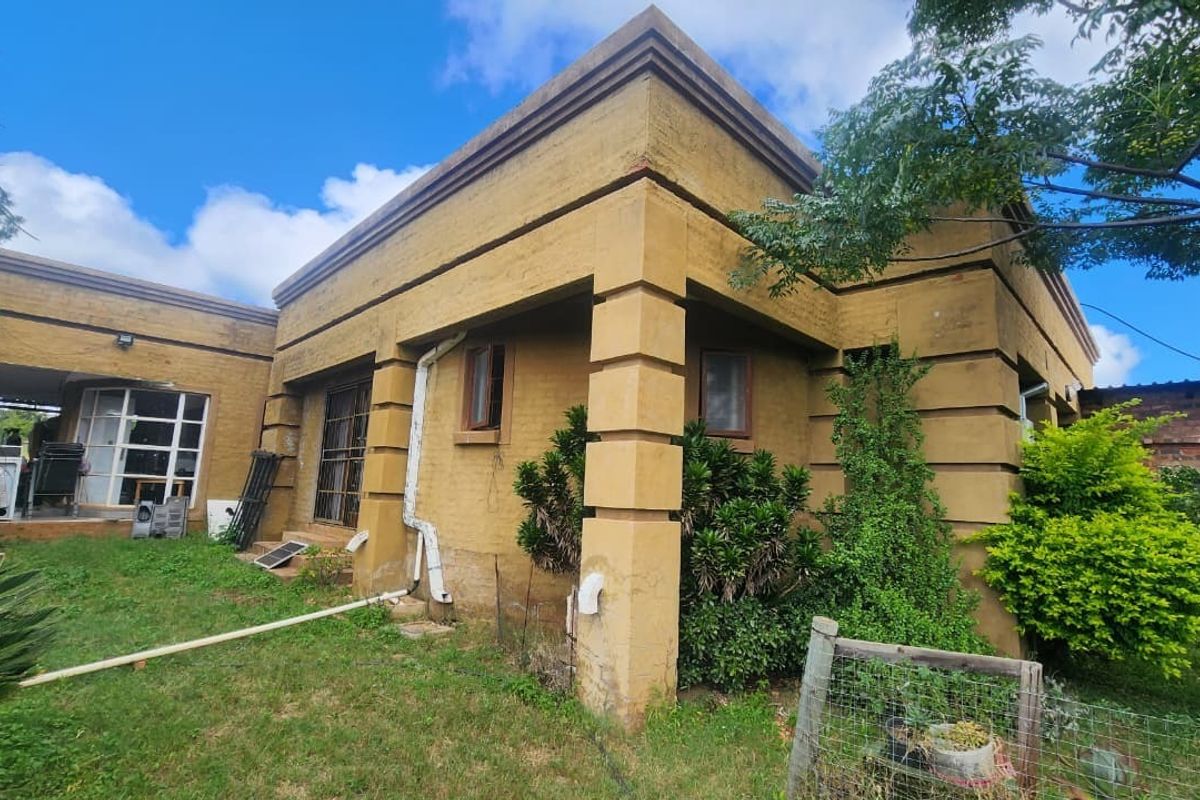 Rear view of a small holding dwelling featuring a plastered facade, covered patio area, and established garden surroundings.