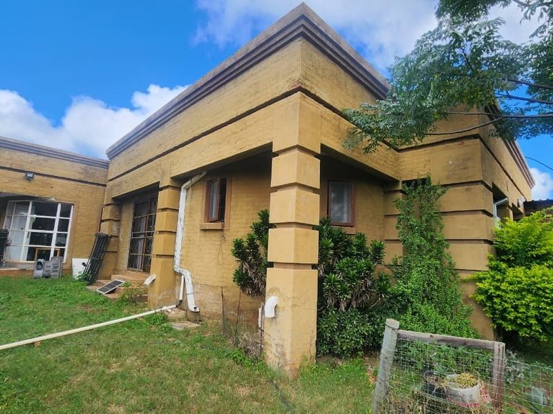 Rear view of a small holding dwelling featuring a plastered facade, covered patio area, and established garden surroundings.