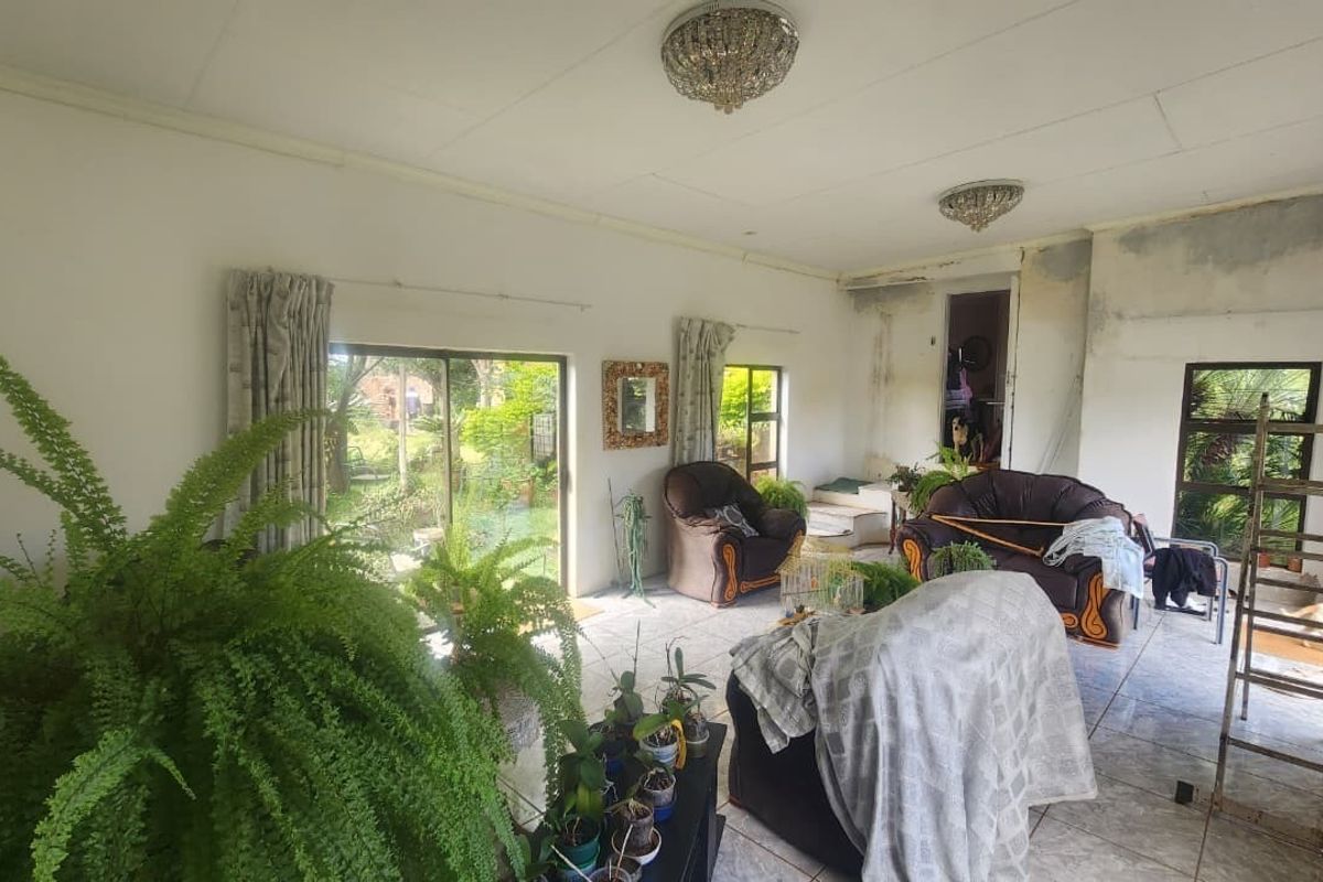 Spacious living area featuring tiled flooring, large sliding glass doors providing garden access, and crystal chandeliers, requiring cosmetic wall repairs and finishing.