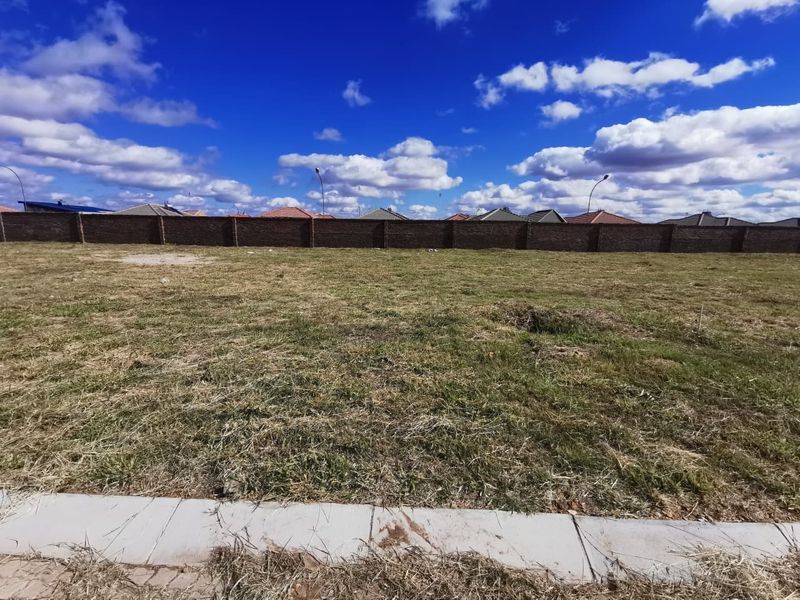 A vacant residential plot featuring a level grass surface and a secure perimeter brick wall, ready for development.