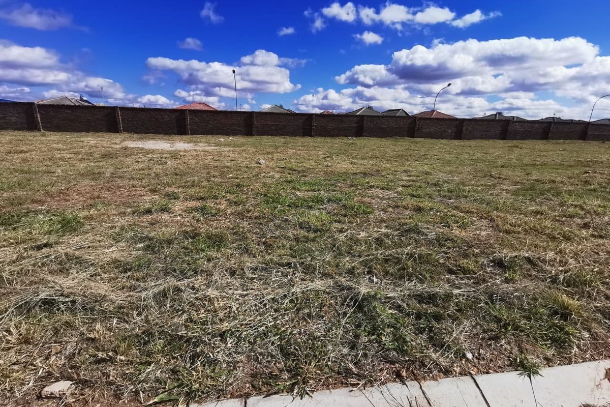 A vacant residential plot featuring a perimeter brick wall and concrete curb, ready for development.