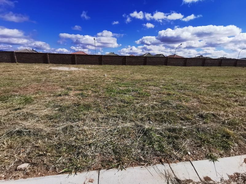 A vacant residential plot featuring a perimeter brick wall and concrete curb, ready for development.