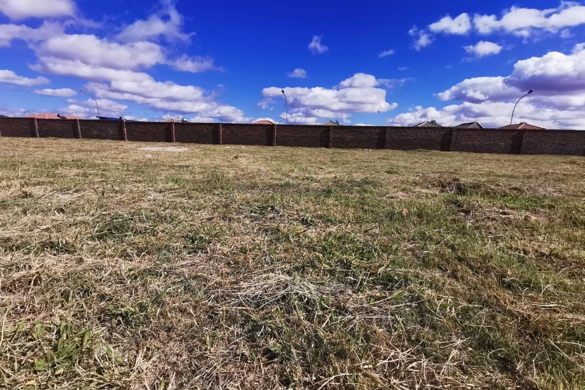 A vacant residential plot featuring a level grass surface and a secure brick perimeter wall.