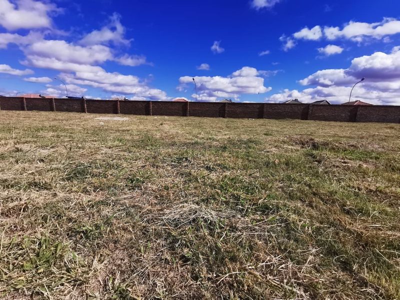 A vacant residential plot featuring a level grass surface and a secure brick perimeter wall.