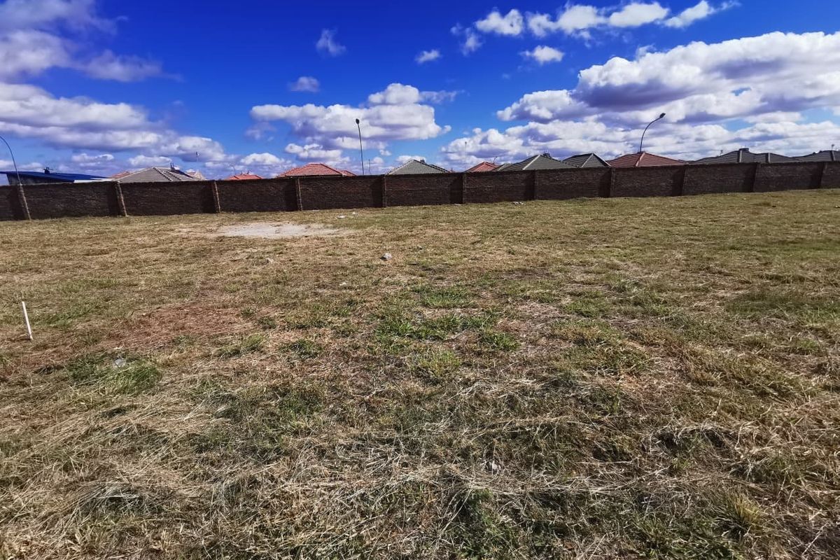 A vacant residential plot featuring a level grass surface and a secure perimeter brick wall, offering a clear space for future development.