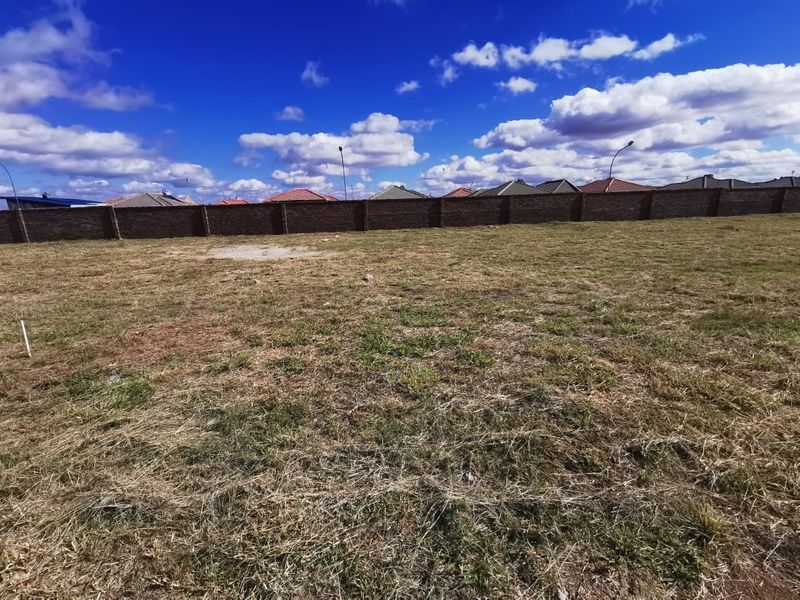 A vacant residential plot featuring a level grass surface and a secure perimeter brick wall, offering a clear space for future development.