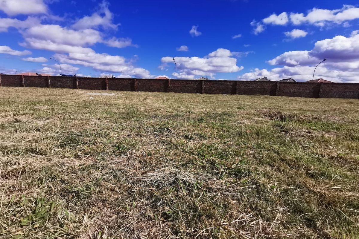 A vacant residential plot featuring a level grass surface enclosed by a solid brick perimeter wall.