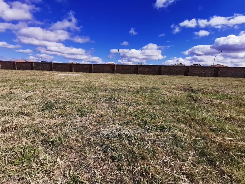 A vacant residential plot featuring a level grass surface enclosed by a solid brick perimeter wall.