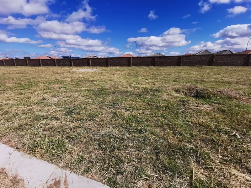 A vacant residential plot featuring a level grass surface and a secure perimeter brick wall.