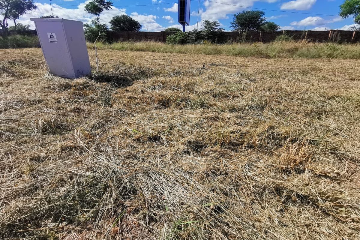 A vacant residential plot featuring dry grass, a perimeter brick wall, and an installed electrical distribution box.