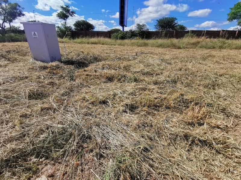 A vacant residential plot featuring dry grass, a perimeter brick wall, and an installed electrical distribution box.