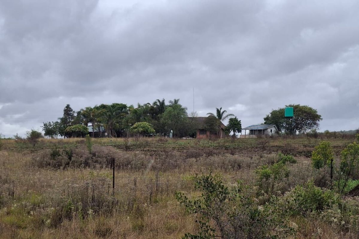 A distant view of the small holding property featuring a main dwelling, outbuildings, and a water tank set within a rural landscape.
