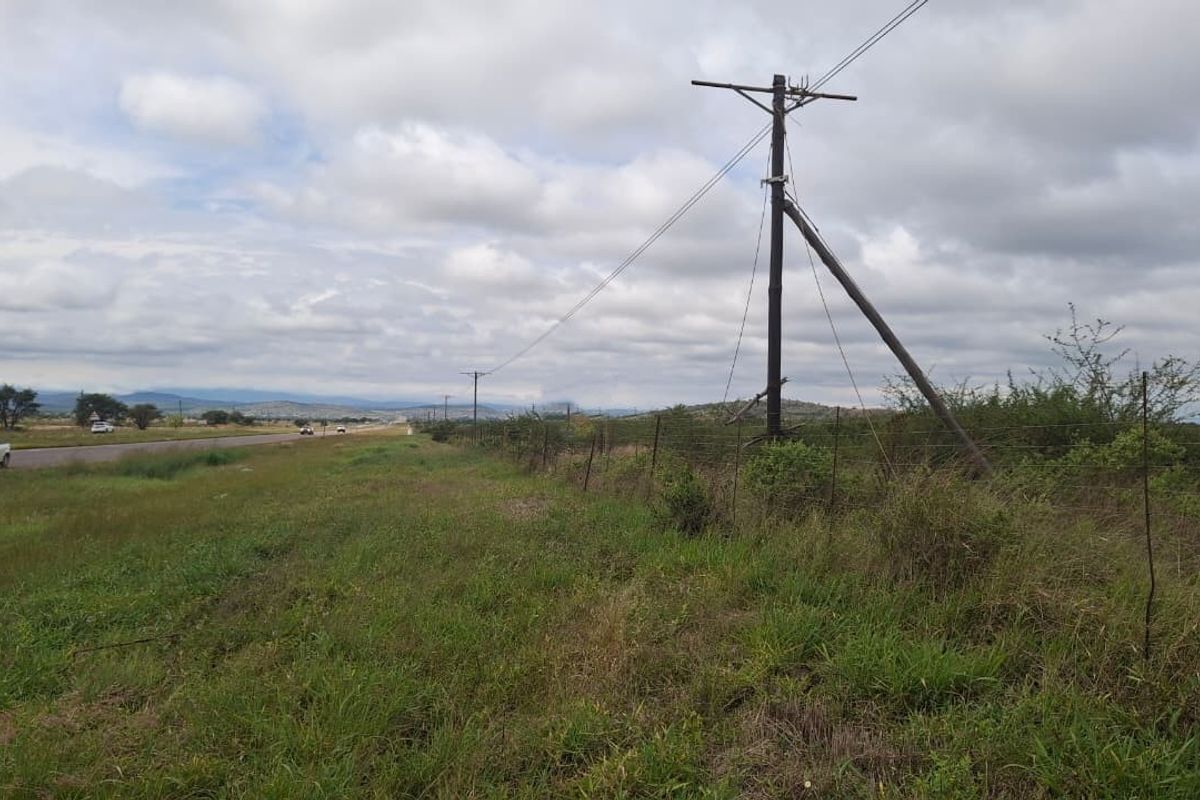 A view of the vacant land parcel adjacent to the main road, featuring existing utility infrastructure and perimeter wire fencing.