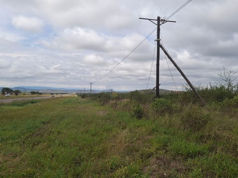 A view of the vacant land parcel adjacent to the main road, featuring existing utility infrastructure and perimeter wire fencing.