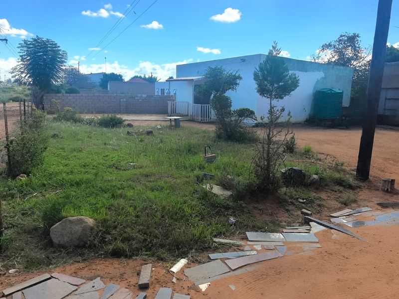 Front view of a residential property featuring an unpaved driveway, boundary wall, and water tank on a spacious plot.