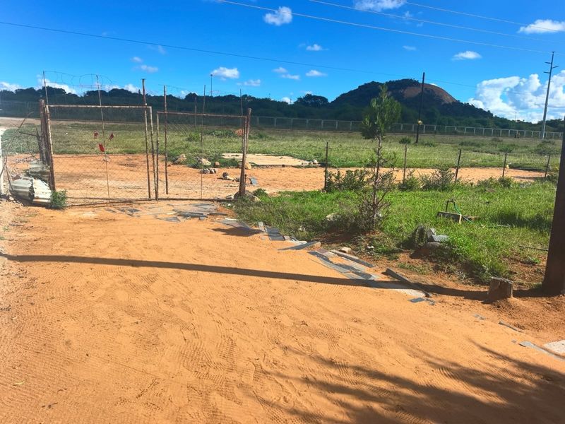 Vacant residential land featuring a metal gate, wire fencing, and an unpaved driveway with mountain views in the background.
