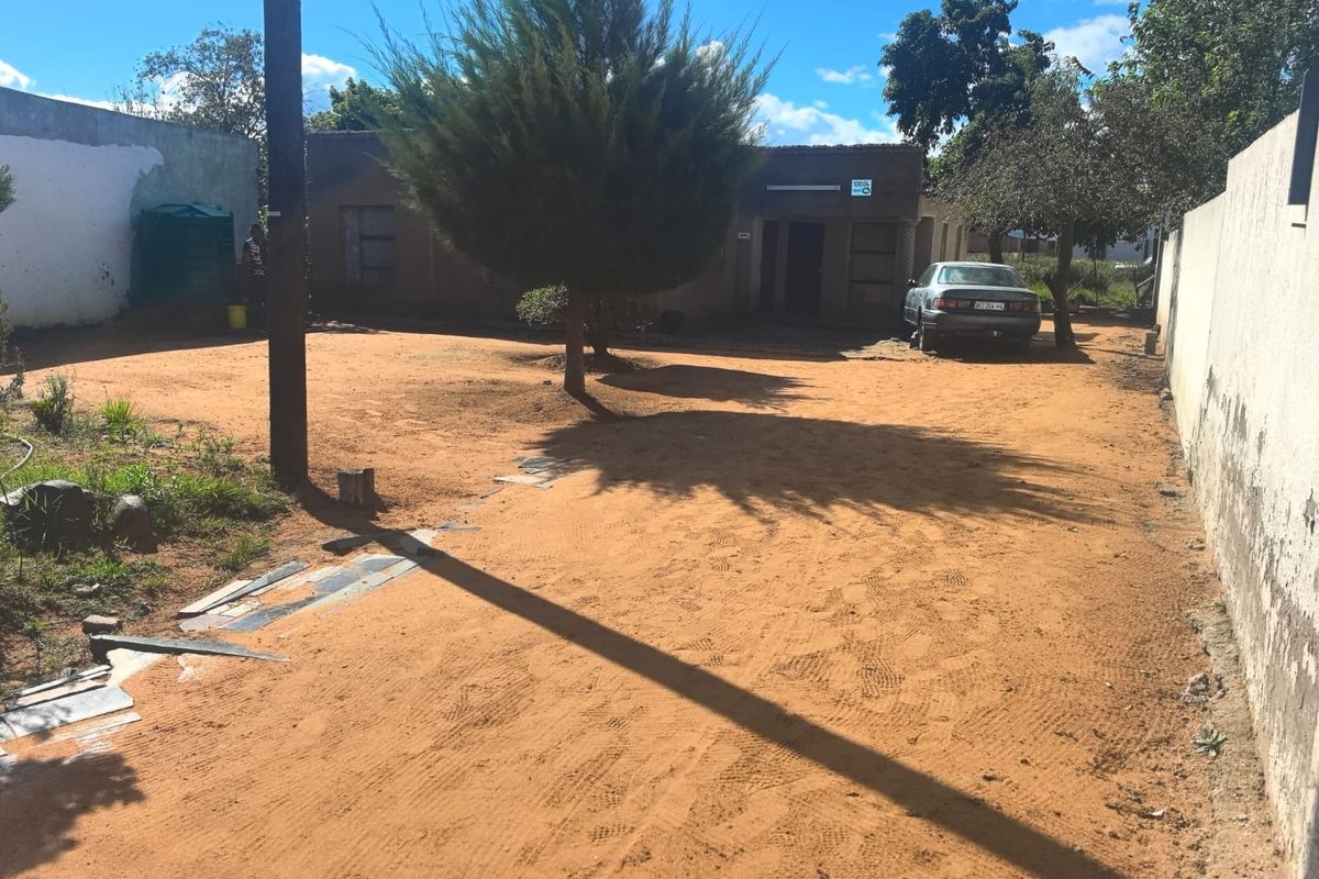 Front view of a residential property featuring an unpaved driveway, perimeter boundary walls, and a water storage tank on a spacious plot.