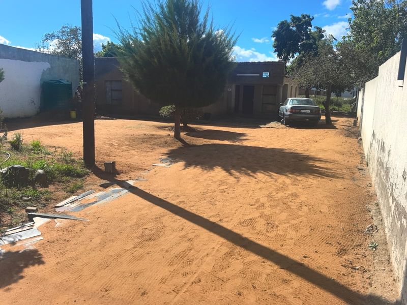 Front view of a residential property featuring an unpaved driveway, perimeter boundary walls, and a water storage tank on a spacious plot.