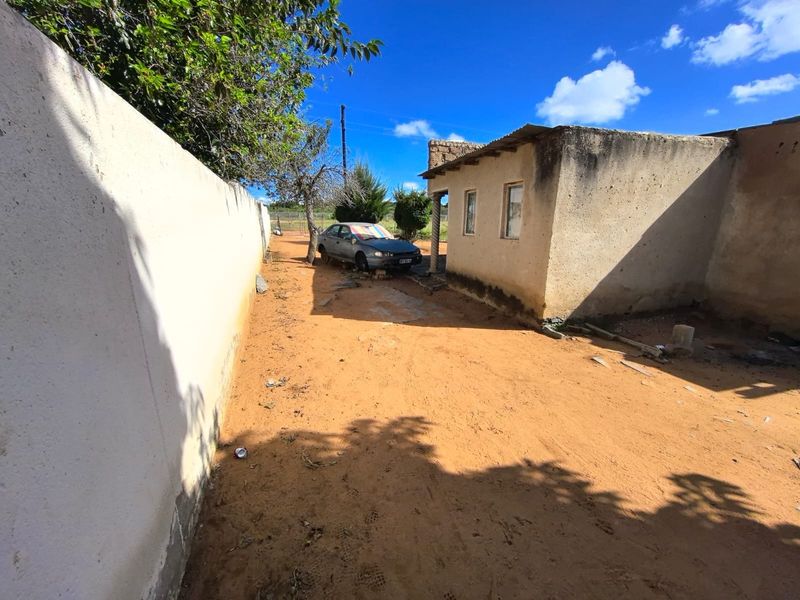Rear exterior view of the property showing a basic structure with a corrugated metal roof and a surrounding boundary wall on an unpaved lot.
