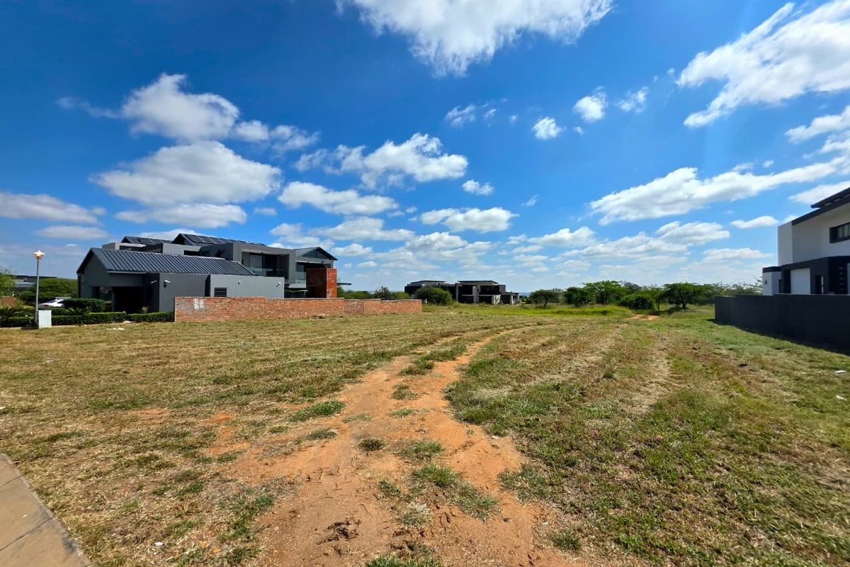 A vacant residential plot featuring a brick boundary wall, situated in a developed estate with surrounding modern homes.