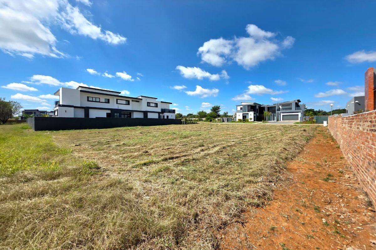 A vacant residential plot featuring a cleared grass surface, enclosed by a brick perimeter wall, situated within a developed residential estate.