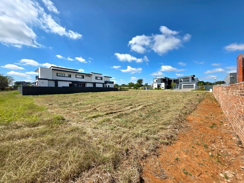 A vacant residential plot featuring a cleared grass surface, enclosed by a brick perimeter wall, situated within a developed residential estate.