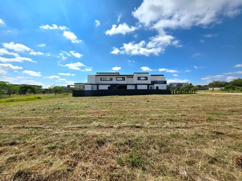 A wide-angle view of a modern residential property set against a large, open vacant plot of land under a clear blue sky.