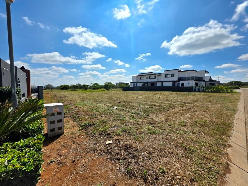 A vacant residential plot featuring level ground, established street infrastructure, and clear views of neighboring modern developments.