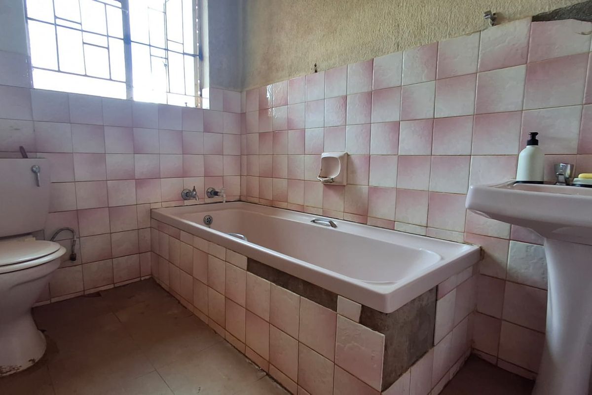 A dated bathroom featuring a bathtub, pedestal sink, and toilet, with significant tile damage and wall finish deterioration requiring renovation.