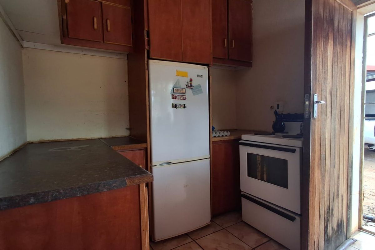 A compact kitchen featuring dated wooden cabinetry, laminate countertops, and tiled flooring, with direct access to an exterior security gate.