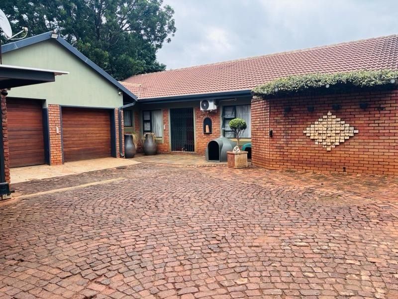 Front exterior view of a house featuring a double garage, brick paved driveway, and a classic exposed brick facade with a tiled roof.