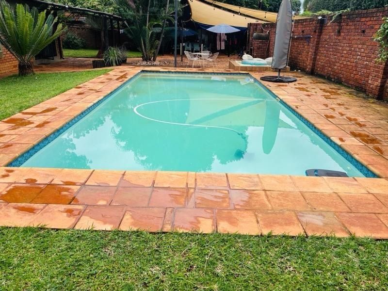 Outdoor swimming pool area featuring terracotta coping, a surrounding lawn, and a brick boundary wall.