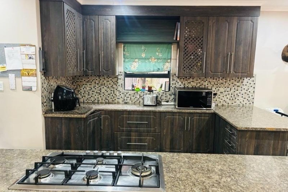 A functional kitchen featuring dark wood cabinetry, granite countertops, a mosaic tile backsplash, and a built-in gas hob on the central island.
