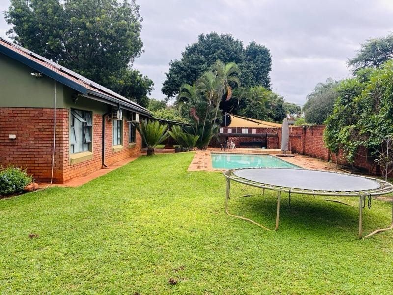 Rear garden view featuring a swimming pool, established lawn, and brick exterior facade of the house.