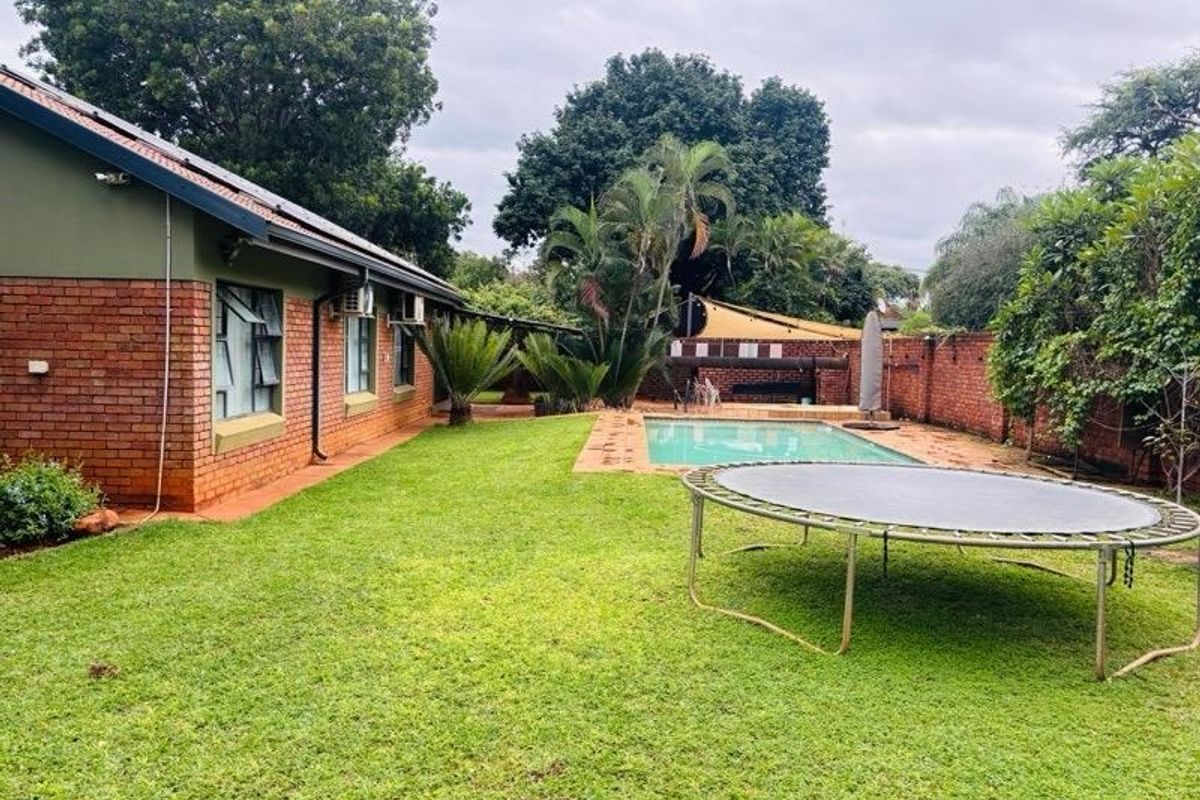 Rear garden view featuring a swimming pool, established lawn, and brick exterior facade of the house.