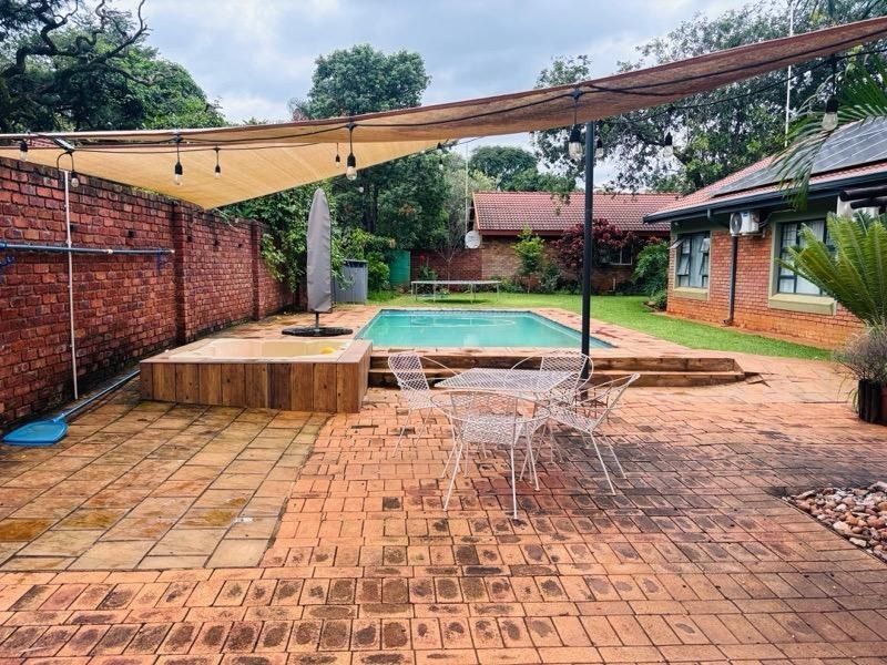 Outdoor entertainment area featuring a swimming pool, built-in jacuzzi, brick paving, and a shade sail, set within a private garden space.
