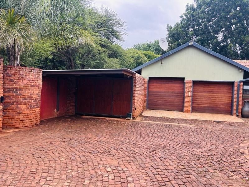 A functional exterior view featuring a double garage with wooden doors, an attached carport, and a paved driveway area.