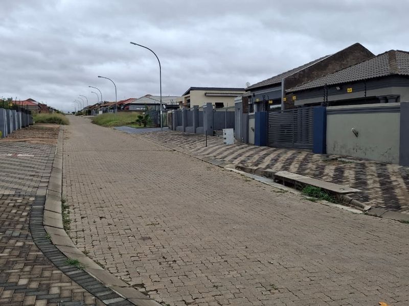 A view of a residential street featuring paved roads, sidewalks, and modern perimeter walls with electric fencing in a suburban estate.