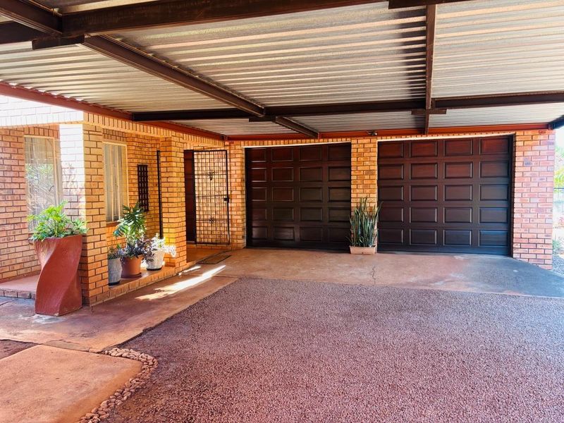 A well-maintained double garage featuring exposed brick walls, a corrugated metal roof, and secure access gates, providing ample covered parking space.
